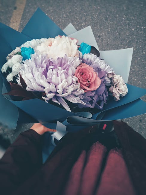 A floral bouquet featuring a large cluster of white chrysanthemum flowers with delicate, densely packed petals, accented by soft pink roses with tightly curled petals, and smaller purple and teal flow