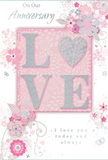 The card shown is a tender tribute to lasting romance, its design blending soft pastel pinks, silvery greys, and creamy whites into a composition as gentle as a walk through Totteridge's leafy lanes in early spring. At the centre, the word "LOVE" is spelled out in raised, softly shimmering glitter, each letter textured so that it almost seems carved from frosted light. The "O" is replaced by a gleaming silver heart, subtly faceted with texture that catches the light and stands out as the visual jewel of the card-like the key bloom in a hand-picked bouquet. Surrounding this focal motif, a cloud of delicate blossoms unfurls in blush and mauve tones, their petals soft and almost watercolour in appearance. Fine, flowing outlines define each bloom, giving the flowers a sense of lightness and motion, as though a gentle breeze from the gardens of Totteridge Valley had been captured on paper. Between the florals, tiny flourishes-curved petals, romantic swirls, and small, graceful butterflies-add a playful, whimsical energy without disturbing the overall serenity. The background is a smooth, muted pink, offering a warm base that allows the silvers and whites to glow. Written in elegant script above and below the design are the words "On Our Anniversary" and "I love you today and always," the lettering slim and poised, like a handwritten note slipped into a bouquet delivered to a Totteridge home. The entire card radiates intimacy and celebration, perfectly suited to accompany anniversary flowers, speaking softly yet with heartfelt conviction of shared years and cherished memories.